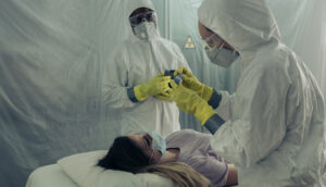 Healthcare workers in full personal protection equipment helping a patient with a virus
